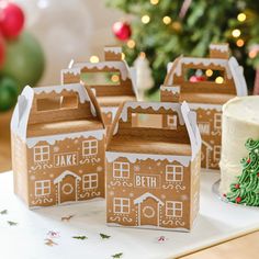 three boxes with gingerbread houses on them sitting next to a christmas tree and cake