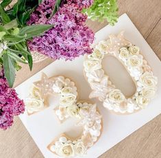 two decorated cookies sitting on top of a table next to purple and white hydrangeas