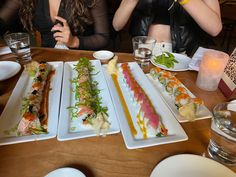 three women sitting at a table with plates of food on it and drinks in front of them