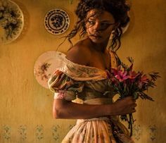 a woman with flowers in her hand and plates on the wall behind her, holding a bouquet of flowers