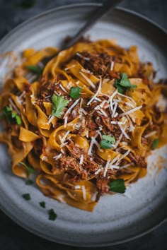 a white plate topped with pasta covered in meat and cheese next to a fork on top of a table