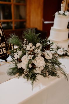 a table topped with a white cake and lots of greenery next to a sign