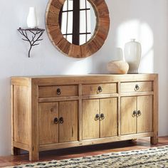 a large wooden dresser sitting next to a round mirror on top of a white wall