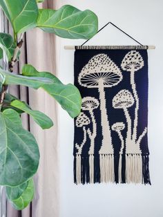 a wall hanging with mushrooms on it next to a potted plant and window curtain