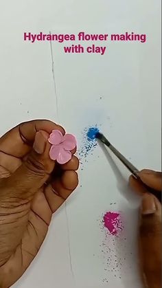 a person is painting flowers on a piece of white paper with pink and blue paint