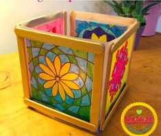 three square stained glass vases sitting on top of a wooden table next to a potted plant