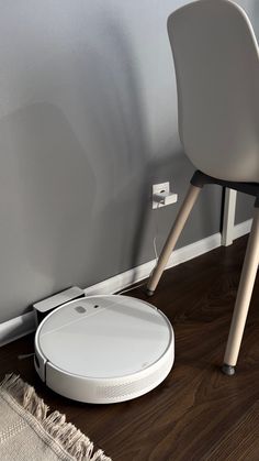 a white roomba sitting on top of a wooden floor next to a gray chair