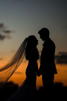 a bride and groom are silhouetted against the sunset