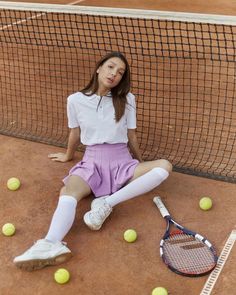 a woman sitting on the ground with tennis balls and racket in front of her