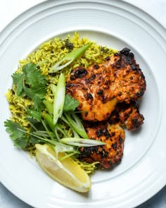 a white plate topped with chicken and rice covered in cilantro next to a lemon wedge