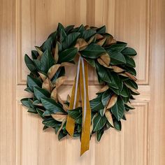 a green wreath with two yellow ribbons hanging on the front door, next to a pair of scissors