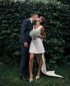 a bride and groom kissing in front of a hedge