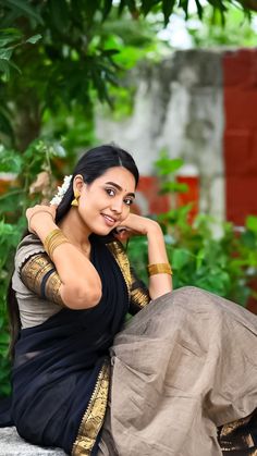 a woman sitting on top of a stone wall wearing a black and gold sari