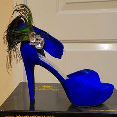 a pair of blue high heels with a peacock feather decoration on the heel, sitting on top of a black box