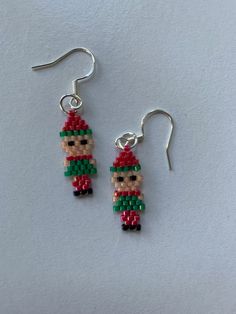 beaded earrings Christmas beaded earrings elf earrings red green peach delica beads elf shaped earrings Christmas elf dangly earrings This is a pair of beaded earrings. In fact, these are Christmas beaded earrings! These elf earrings are made from red, green, peach and black delica beads, which have been woven together using brick stitch into elf shaped earrings. A great pair of Christmas elf earrings. These dangly earrings can bring you a little Christmas cheer! The earrings are completed with Christmas Seed Bead Earrings, Beadcraft Ideas, Beaded Christmas Earrings, Christmas Beaded Earrings, Weaving Earrings, Brick Stitch Pattern Earring, Elf Earrings, Christmas Beading, Beaded Ideas