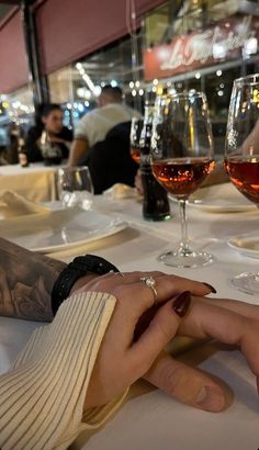 two people holding hands at a table with glasses of wine in front of them,