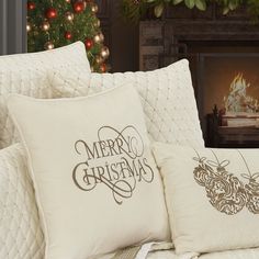 two pillows sitting on top of a couch next to a christmas tree in front of a fireplace