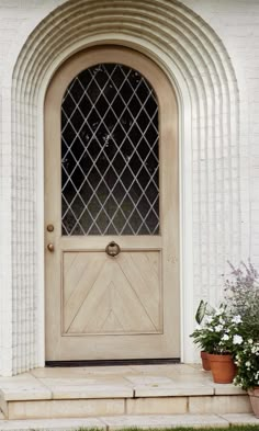 a wooden door sitting on the side of a white brick building next to potted plants