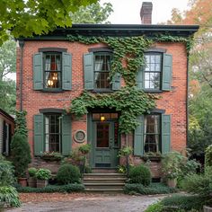 an old brick house with green shutters and ivy growing on the front door, surrounded by greenery