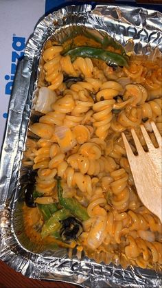 a metal pan filled with macaroni and cheese next to a wooden spoon on top of aluminum foil