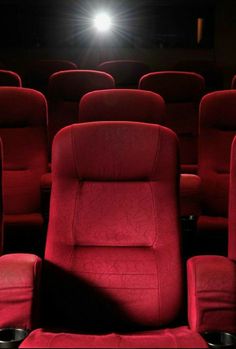 an empty theater with red seats and a bright light shining on the wall behind them