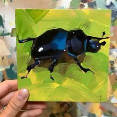 a painting of a blue beetle is being held up by a person's hand