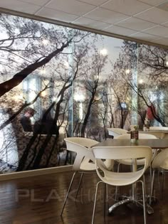 an empty restaurant with tables and chairs in front of a glass wall that has trees painted on it