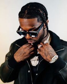 a man wearing sunglasses and a black jacket is tying his hair in a bun with braids