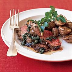 a white plate topped with meat and veggies on top of a red table