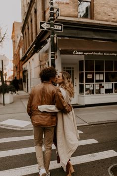 a man and woman walking down the street in front of a store kissing each other