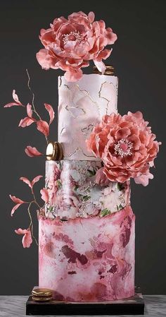 a three tiered cake with pink flowers on top and gold decorations around the edges