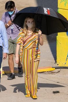 a woman in striped jumpsuits holding an umbrella and wearing a face mask while walking down the street