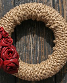 a wreath made out of rope with red roses on it sitting on top of a wooden table