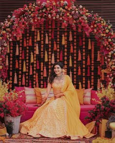 a woman sitting on top of a pink couch in front of a flower covered wall