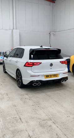 the rear end of a white car parked in a garage with other cars behind it