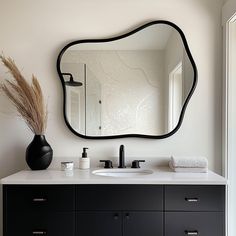 a bathroom vanity with a large mirror above it and a black vase on the counter