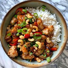 a bowl filled with chicken, cashews and rice on top of a marble table