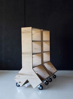 a wooden shelf sitting on top of a white floor next to a black wall with wheels