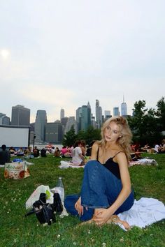 a woman sitting on the grass in front of a city skyline