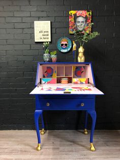 a blue desk with flowers and pictures on the wall behind it in front of a brick wall