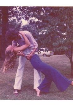 a man and woman are kissing in the grass with trees in the back ground behind them