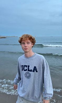 a young man standing on top of a beach next to the ocean