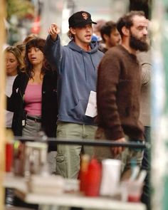 a group of people walking down a street next to each other and one person wearing a hat