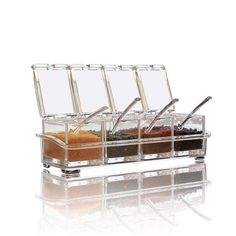 three glass spice containers with spoons and seasoning in them on a white background