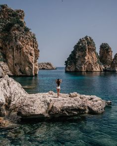 a woman standing on top of a rock next to the ocean with her arms in the air