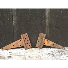 two rusty metal brackets are sitting on a wooden surface, one has holes in it