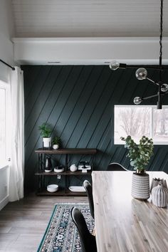 a dining room with green walls and wooden table, black chairs and potted plants