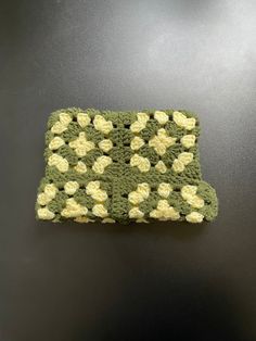 a green and yellow crocheted dishcloth on a black countertop with white flowers