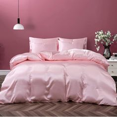 a bed with pink sheets and pillows in front of a purple wall, next to a white dresser