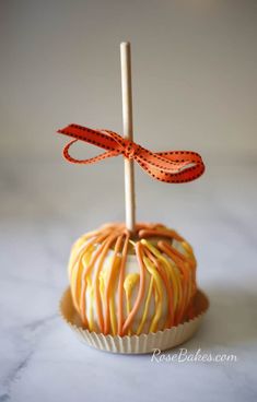 an orange and white candy apple with a red ribbon on it's end, sitting on a marble surface